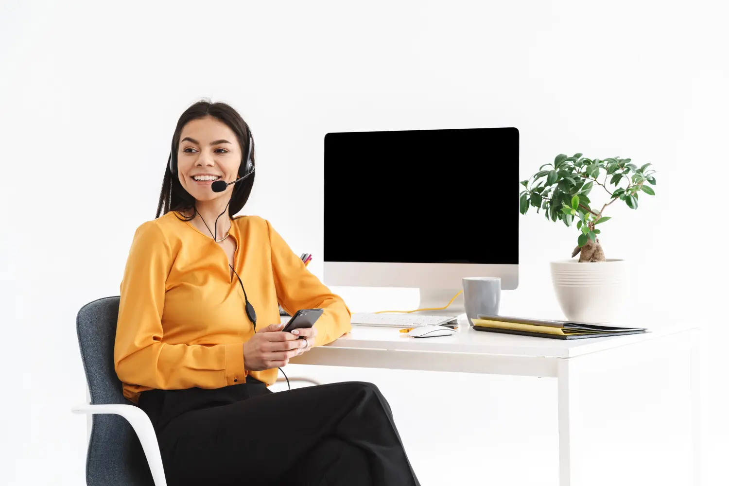 Foto einer kaukasischen Telefonistin, die ein Mikrofon-Headset trägt und ihr Smartphone hält, während sie im Büro arbeitet